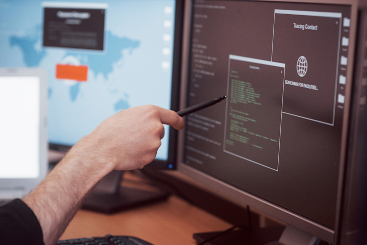 man-uses-a-laptop-computer-with-many-monitors-RP8NT9N