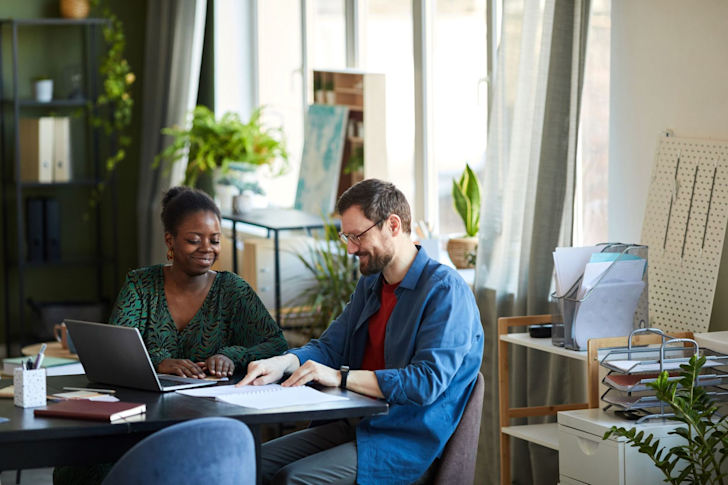 Vrolijke man en vrouw aan het werk achter laptop